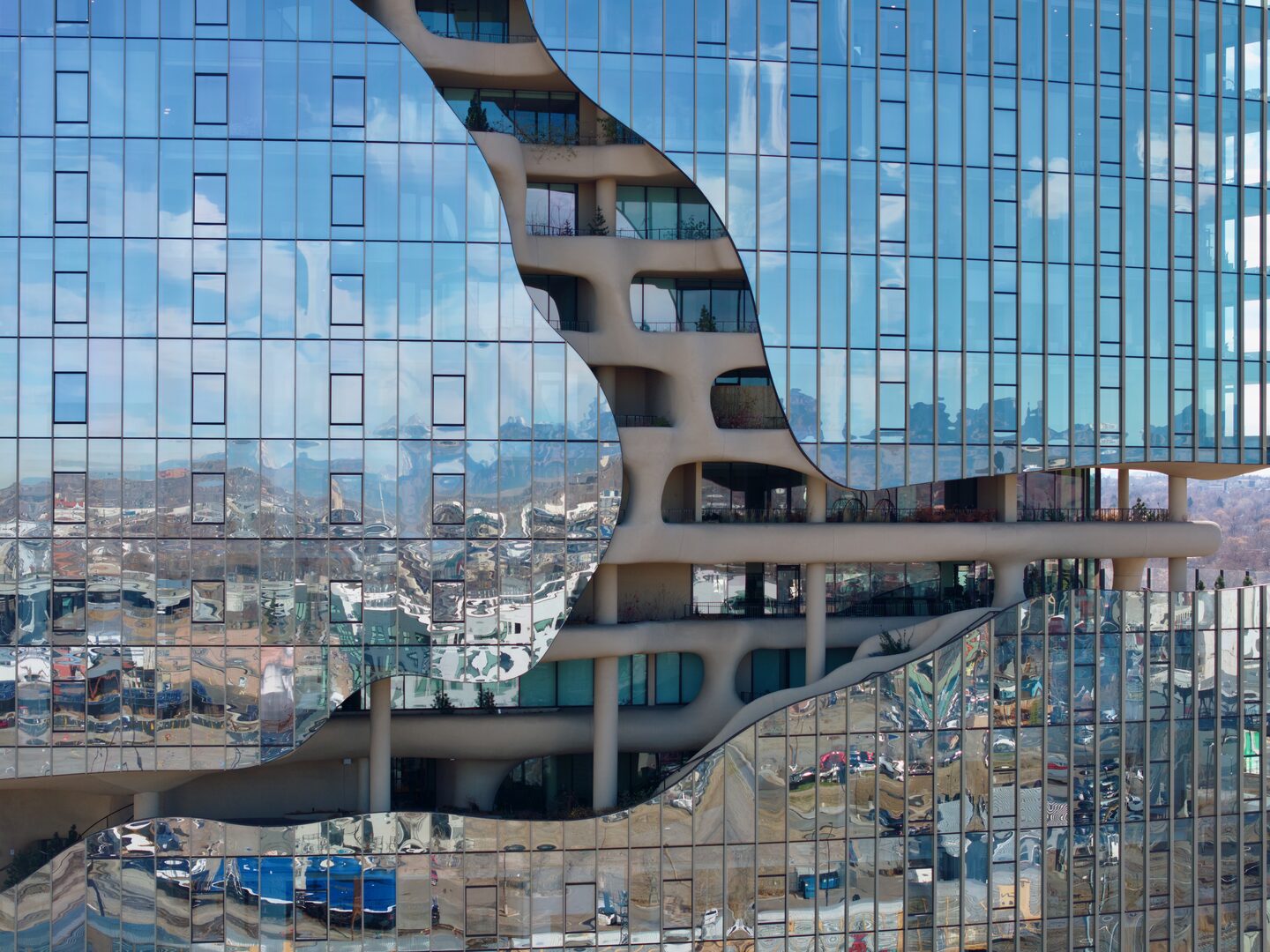 Close-up aerial view of a glass curtain wall office tower with the city skyline reflected in the facade