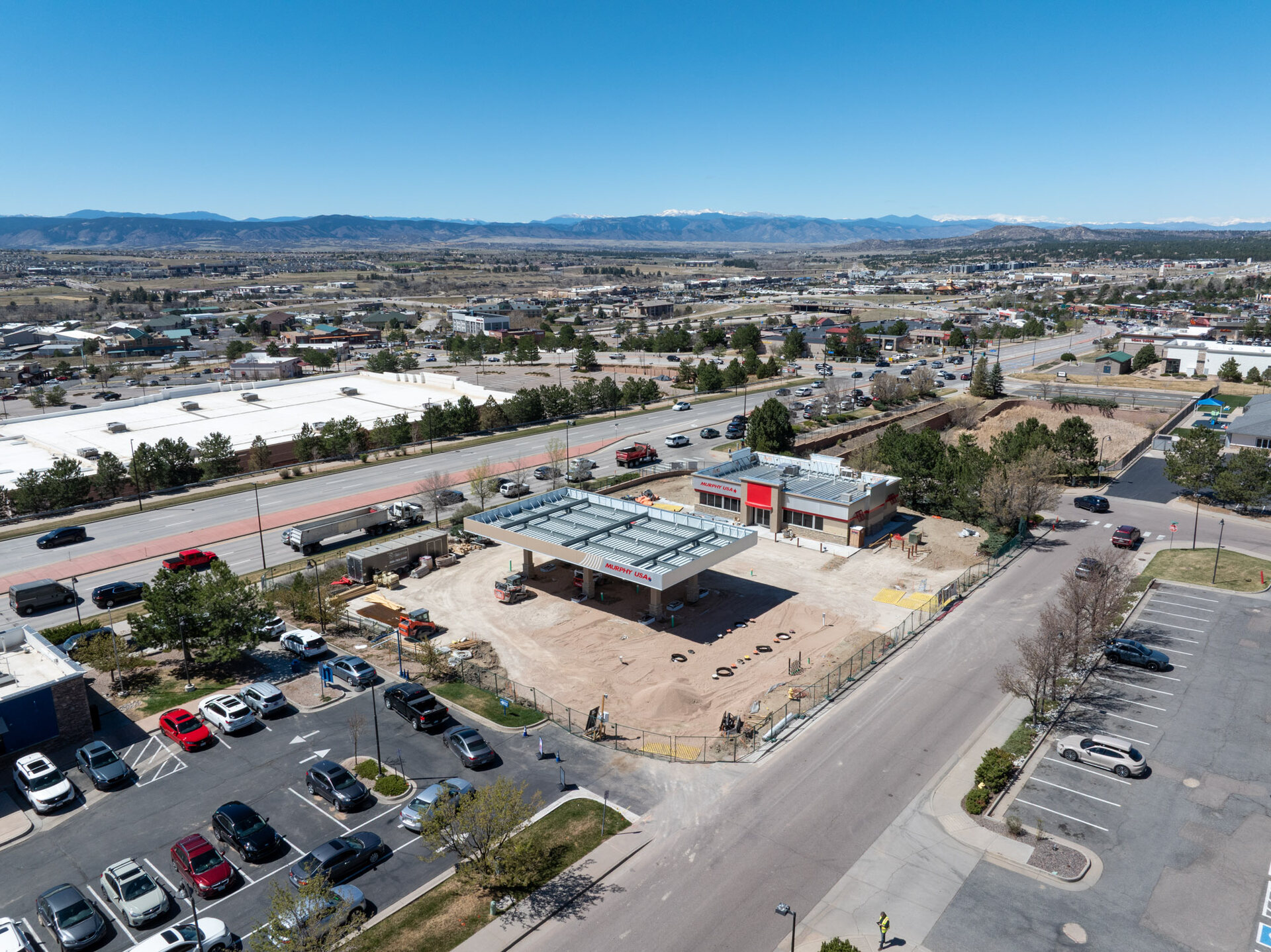 Aerial view of an active commercial construction site with the snow-capped Rampart Range and Colorado Springs extending to the mountains behind