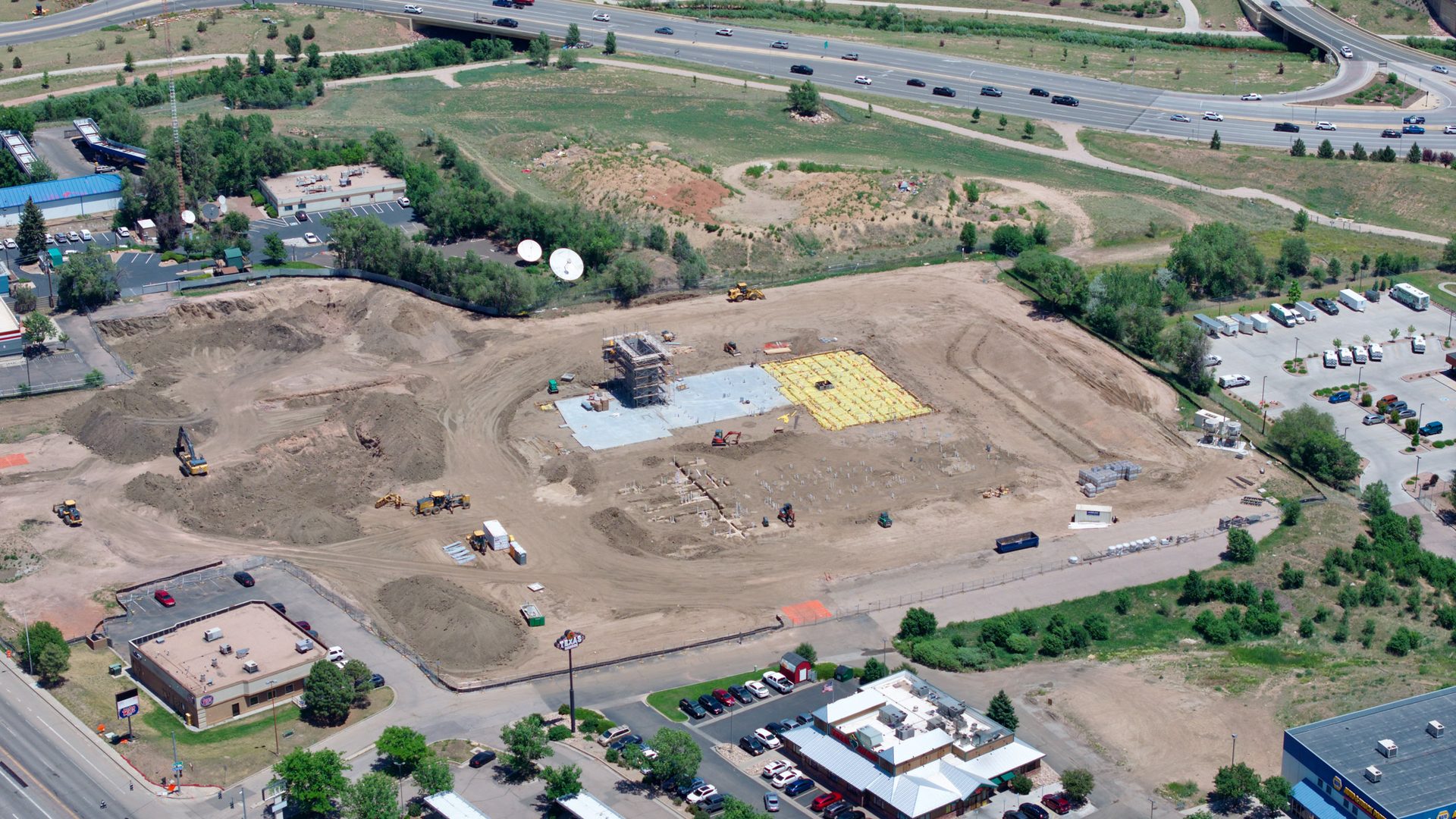 Aerial construction progress documentation showing site grading, foundation work, equipment staging, and surrounding access roads.