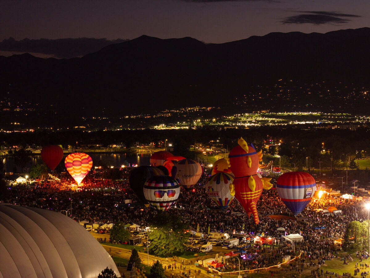 Single hot air balloon glowing amber against the night sky over Colorado Springs