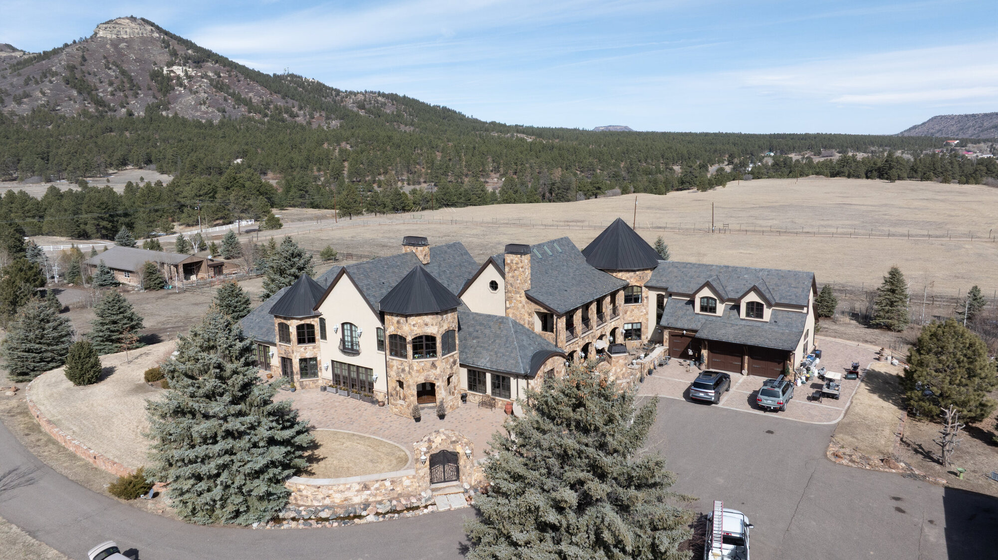 Luxury stone estate in the Colorado foothills — multi-plane roof, circular driveway, mountain backdrop