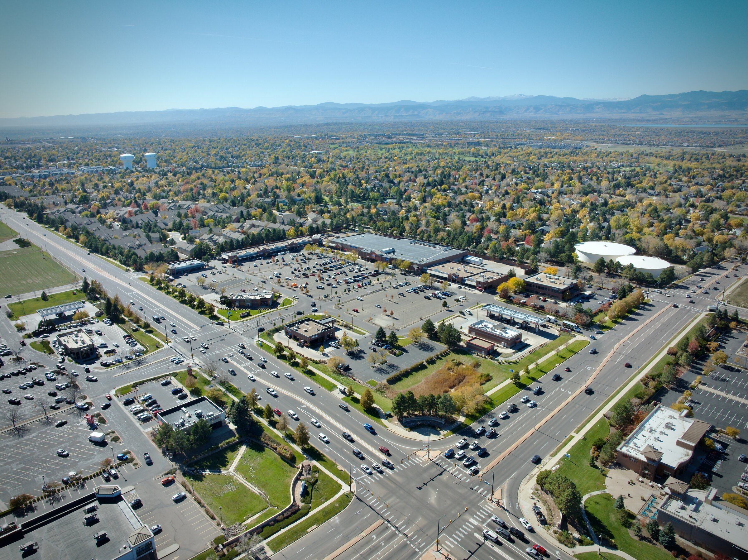 Aerial view of a Colorado residential neighbourhood at peak fall foliage — mature tree canopy in autumn colour, Rocky Mountain backdrop, established community with retail and amenities visible