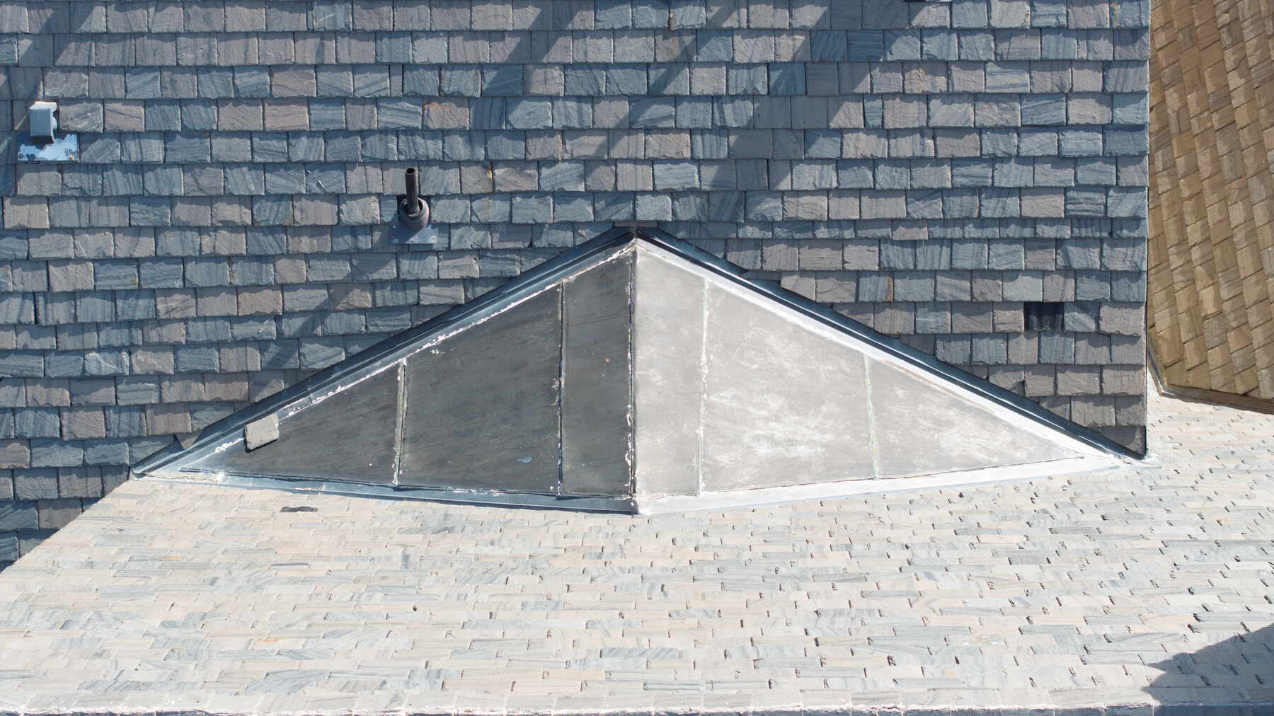 Close-up of slate tile surface condition — individual tiles, skylight flashing, and pipe penetration clearly readable from drone altitude