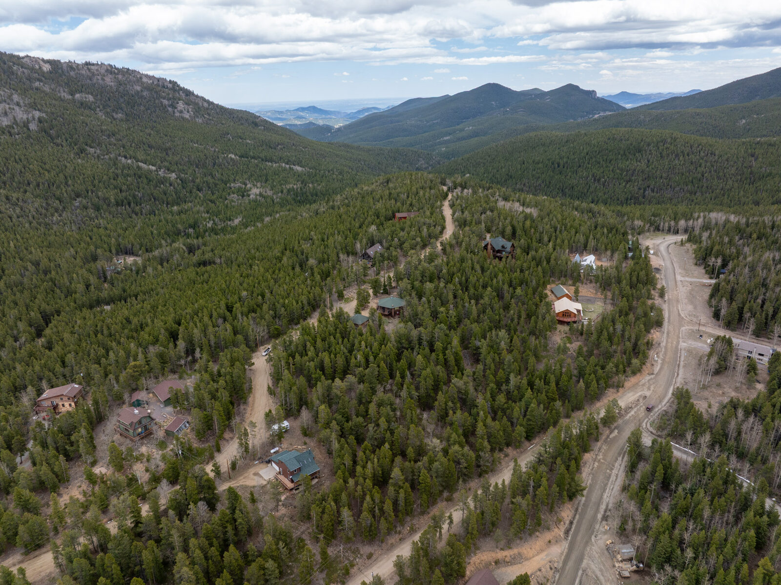 Aerial view of mountain homes nestled in dense Colorado pine forest with layered mountain ranges visible across the valley