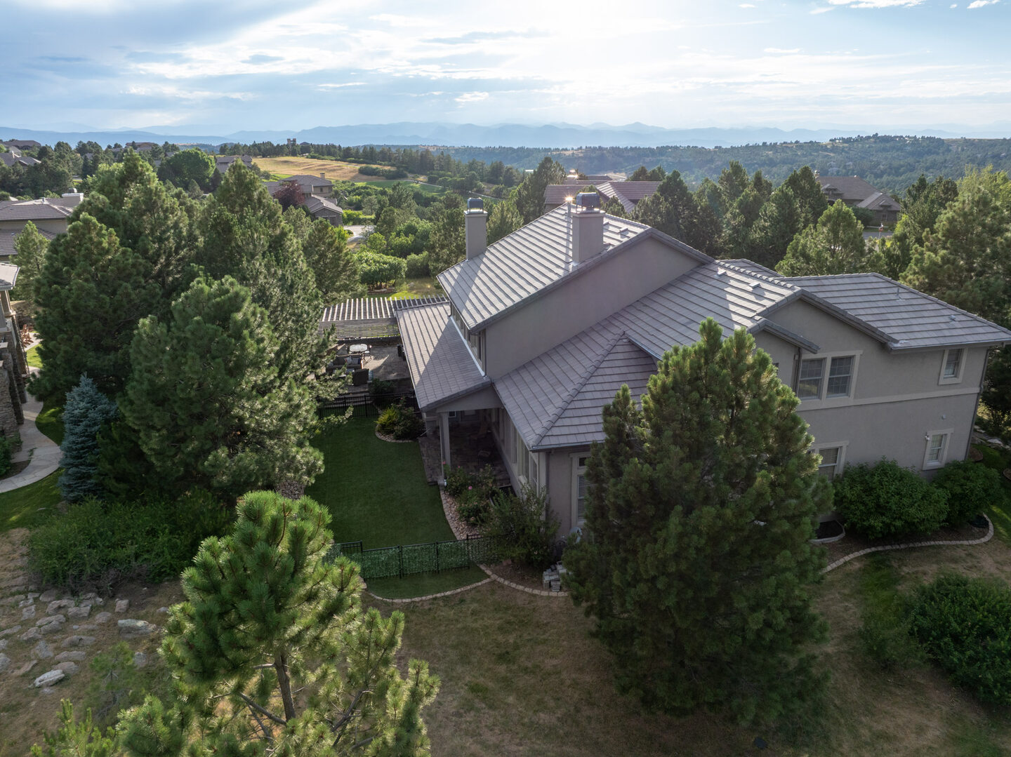 Aerial view of a premium estate home with metal standing-seam roof surrounded by mature Colorado pines, Front Range visible in the distance