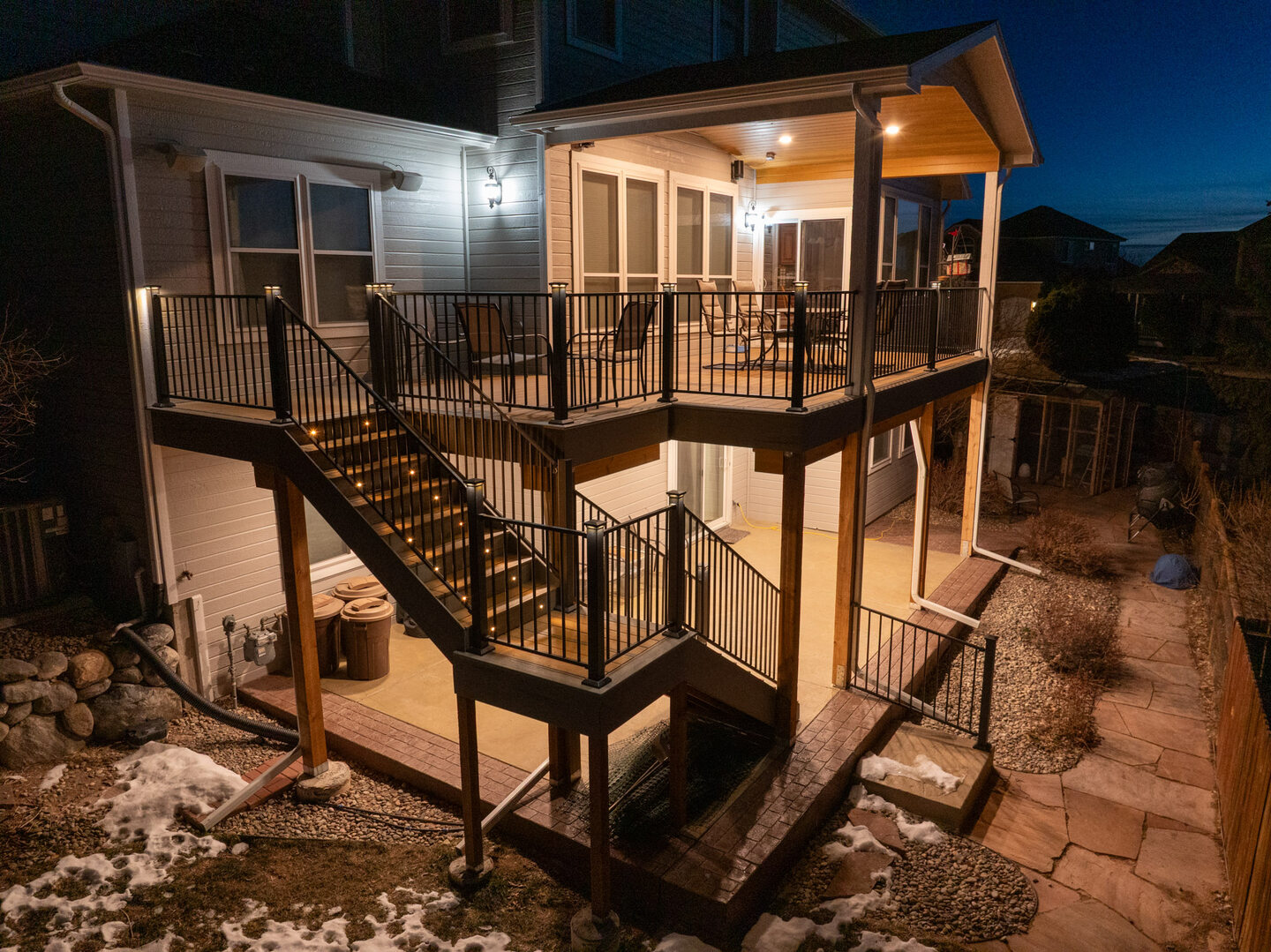 Close aerial view of a two-story deck with warm amber porch lighting at blue hour, Colorado Springs