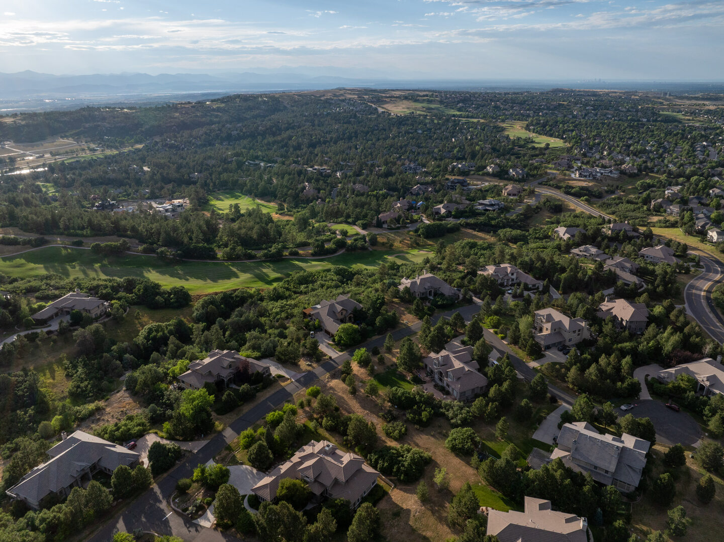 Wide aerial view of a golf-course-adjacent Colorado Springs neighborhood with pine trees and the Front Range beyond