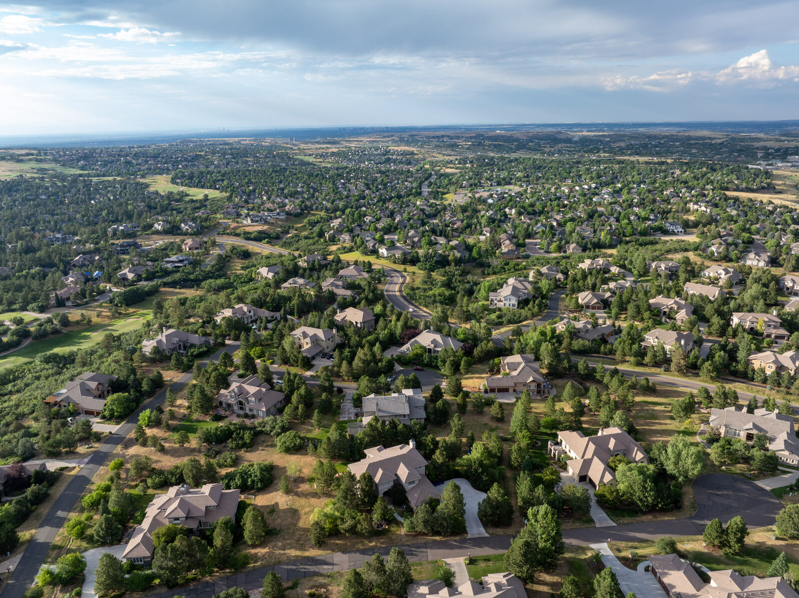 Wide aerial view of a premium Colorado Springs neighborhood beneath a dramatic summer cloudscape