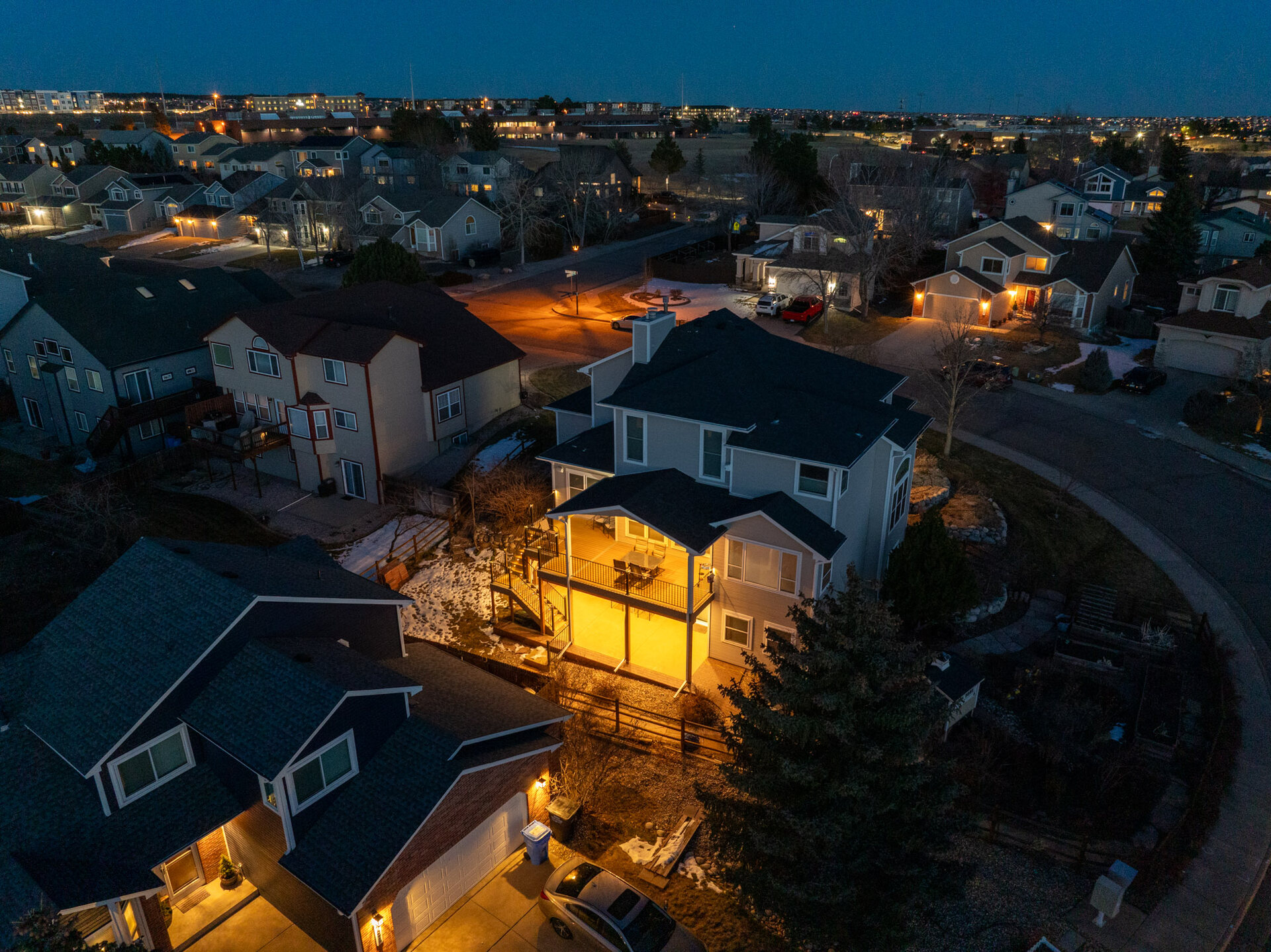 Aerial view of a Colorado Springs neighborhood at blue hour, warm porch lights glowing across the rooftops